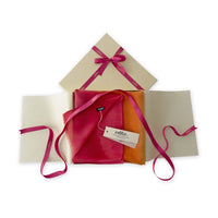 Luxury gift box with a pink ribbon containing a hand-painted Otta pure cashmere scarf on a white background.
