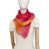 Mannequin wearing an elegant hand-painted Otta pure cashmere scarf on a white background. Warm red, orange and yellow tones.
