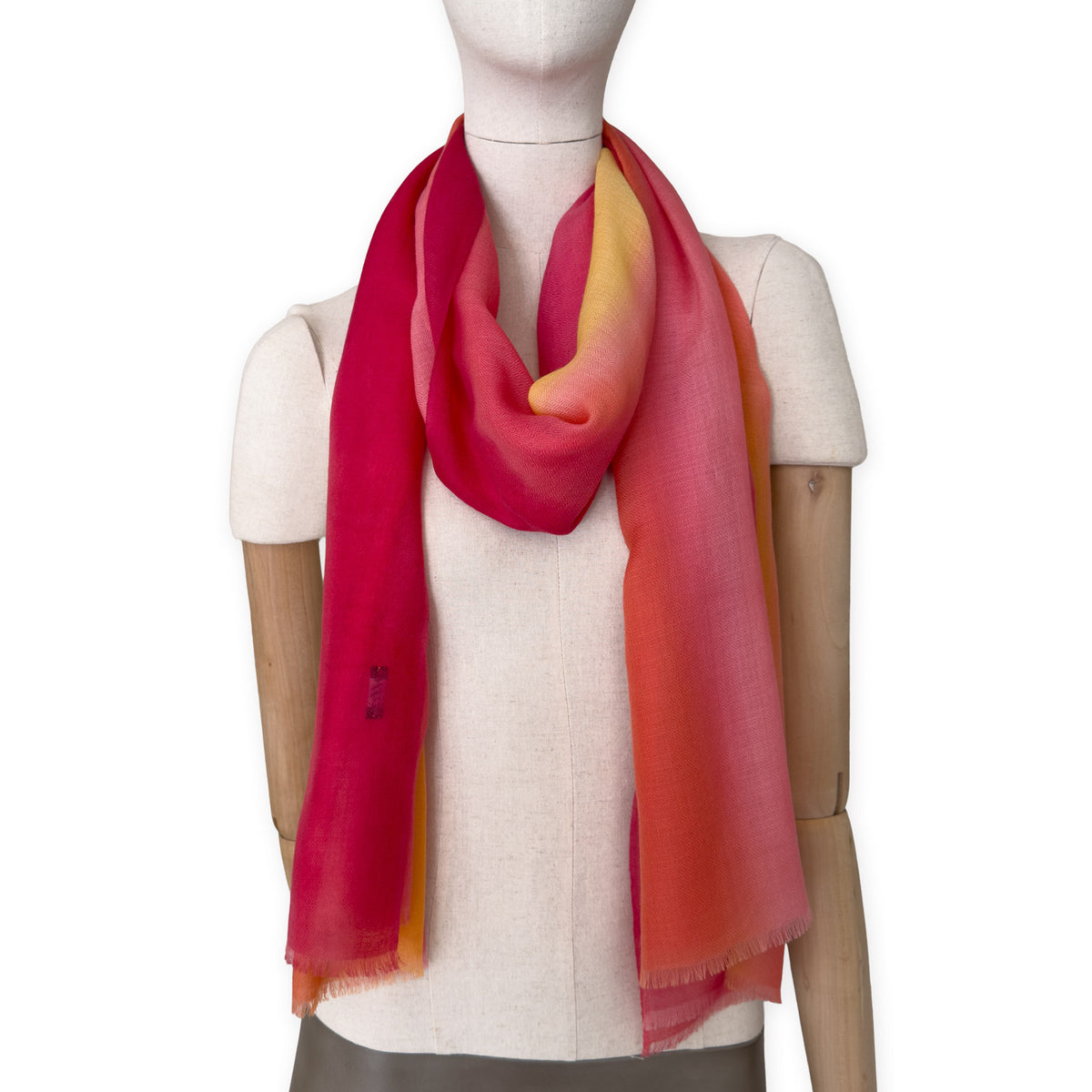 Mannequin wearing an elegant hand-painted Otta pure cashmere scarf on a white background. Warm red, orange and yellow tones.
