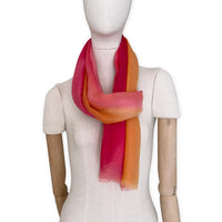 Mannequin wearing an elegant hand-painted Otta pure cashmere scarf on a white background. Warm red, orange and yellow tones.
