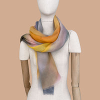 Mannequin wearing a hand-painted pure cashmere scarf by Otta-Italy, beige background. Yellow, orange, pink and gray shades. 69 x 202 cm.
