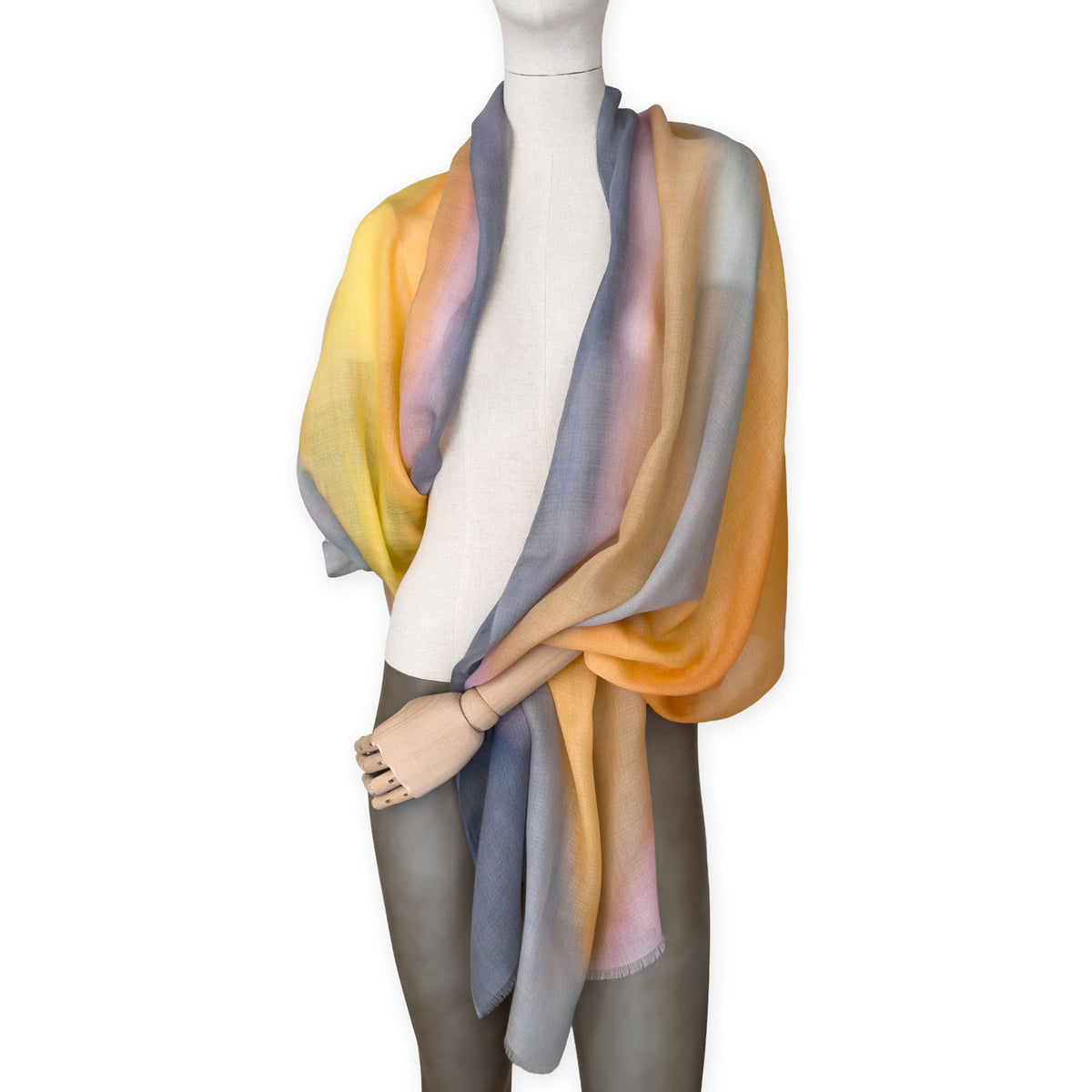 Mannequin wearing an elegant hand-painted Otta pure cashmere scarf on a white background. Warm yellow, orange, pink and gray tones.
