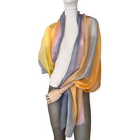 Mannequin wearing an elegant hand-painted Otta pure cashmere scarf on a white background. Warm yellow, orange, pink and gray tones.
