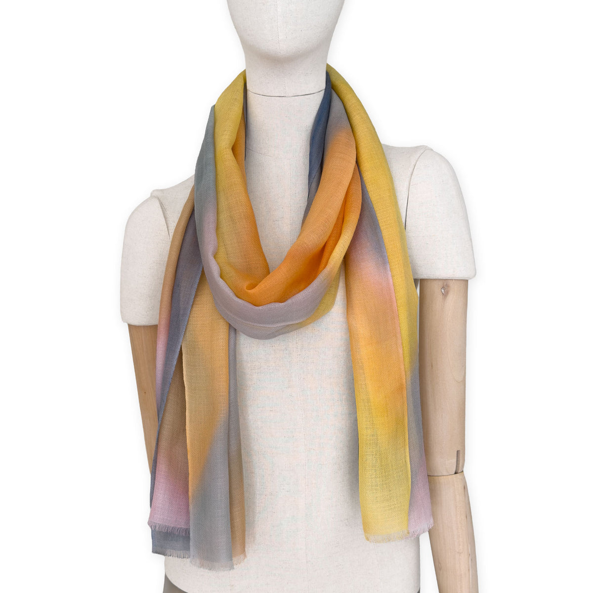 Mannequin wearing an elegant hand-painted Otta pure cashmere scarf on a white background. Warm yellow, orange, pink and gray tones.
