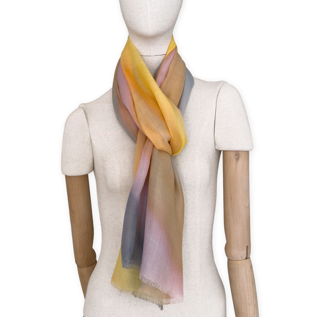 Mannequin wearing an elegant hand-painted Otta pure cashmere scarf on a white background. Warm yellow, orange, pink and gray tones.
