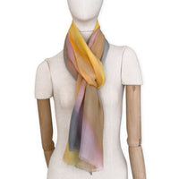 Mannequin wearing an elegant hand-painted Otta pure cashmere scarf on a white background. Warm yellow, orange, pink and gray tones.
