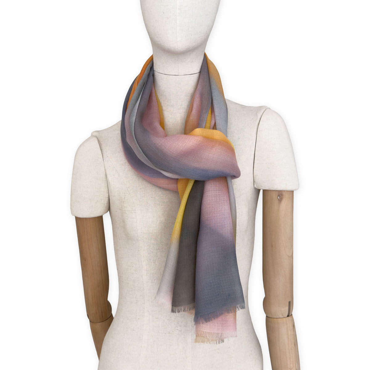 Mannequin wearing an elegant hand-painted Otta pure cashmere scarf on a white background. Warm yellow, orange, pink and gray tones.
