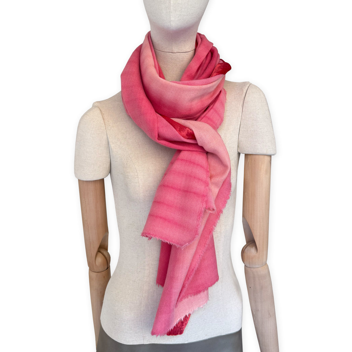 Mannequin wearing a hand-painted Otta cashmere & wool blend scarf on a white background in 
red, fuchsia and pink tones. Lightweight, warm, and elegant accessory measuring 57 x 180 cm. Unique artisan scarf with hand-fringed edges, perfect for women and men.
