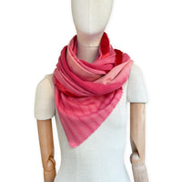 Mannequin wearing a hand-painted Otta cashmere & wool blend scarf on a white background in 
red, fuchsia and pink tones. Lightweight, warm, and elegant accessory measuring 57 x 180 cm. Unique artisan scarf with hand-fringed edges, perfect for women and men.
