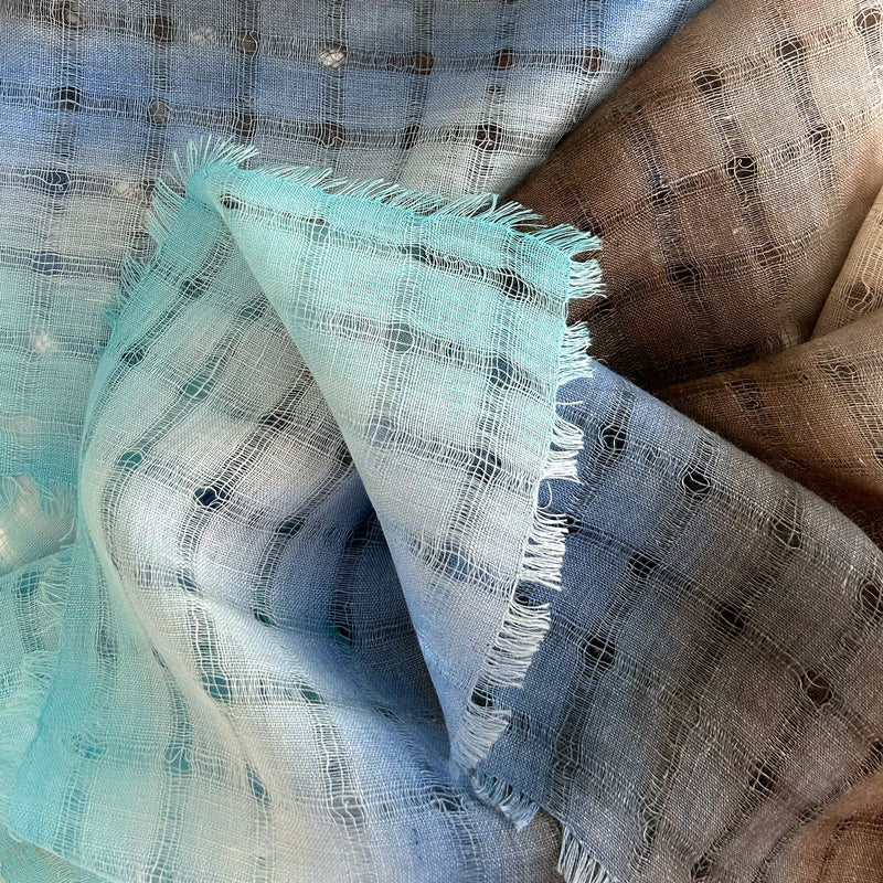 Close-up of a hand-painted Otta-Italy pure linen scarf showcasing its premium open-weave texture with shades of indigo and turquoise alongside delicate hand-fringed edges.