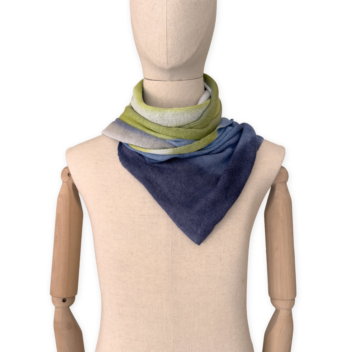 Mannequin wearing a hand-painted Otta pure linen scarf on a white background in 
blue, midnight blue, indigo, light blue, green tones. soft, fresh and lightweight, and elegant accessory measuring 34 x 192 cm. Unique artisan scarf with hand-sewn edges, perfect for women and men.
