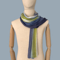 Mannequin wearing scarf on a pastel blue background. Hand-painted linen scarf by Otta-Italy, 34 x 192 cm, featuring 
blue, midnight blue, indigo, light blue, green. Luxury Italian pure linen accessory, soft, fresh and lightweight scarf for women and men.
