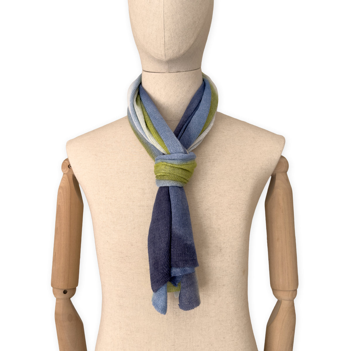 Mannequin wearing a hand-painted Otta pure linen scarf on a white background in 
blue, midnight blue, indigo, light blue, green tones. soft, fresh and lightweight, and elegant accessory measuring 34 x 192 cm. Unique artisan scarf with hand-sewn edges, perfect for women and men.
