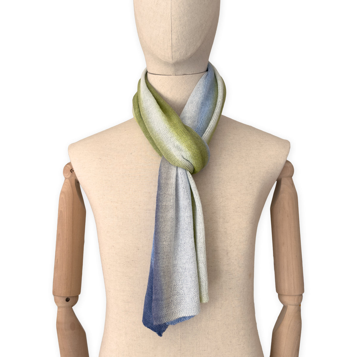 Mannequin wearing a hand-painted Otta pure linen scarf on a white background in 
blue, midnight blue, indigo, light blue, green tones. soft, fresh and lightweight, and elegant accessory measuring 34 x 192 cm. Unique artisan scarf with hand-sewn edges, perfect for women and men.
