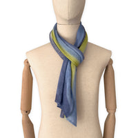 Mannequin wearing a hand-painted Otta pure linen scarf on a white background in 
blue, midnight blue, indigo, light blue, green tones. soft, fresh and lightweight, and elegant accessory measuring 34 x 192 cm. Unique artisan scarf with hand-sewn edges, perfect for women and men.

