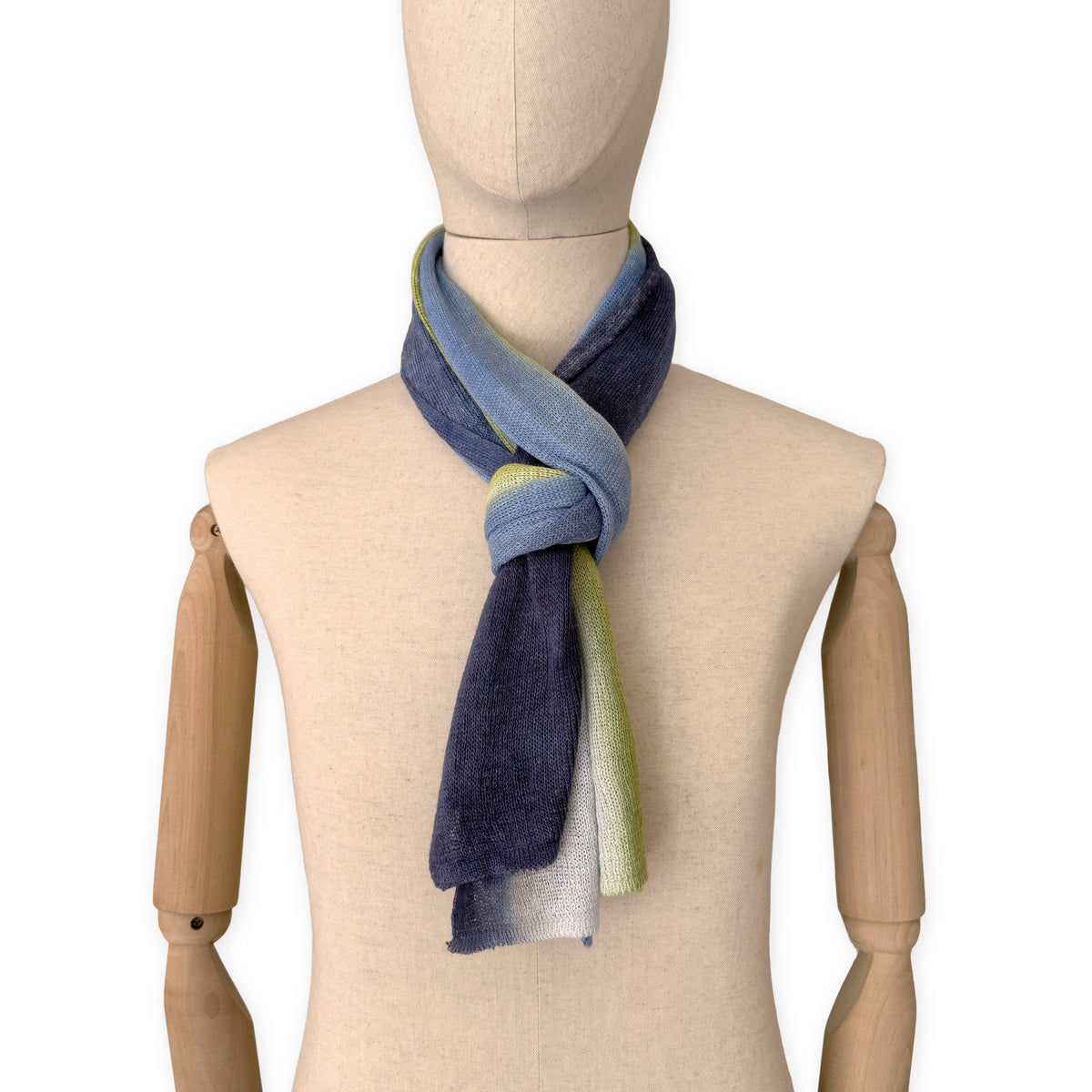 Mannequin wearing a hand-painted Otta pure linen scarf on a white background in 
blue, midnight blue, indigo, light blue, green tones. soft, fresh and lightweight, and elegant accessory measuring 34 x 192 cm. Unique artisan scarf with hand-sewn edges, perfect for women and men.
