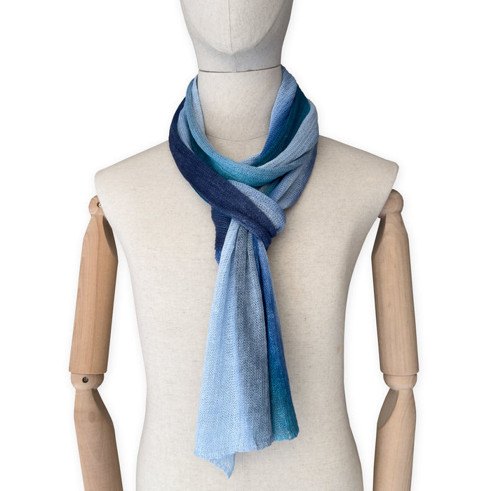 Mannequin wearing a colorful and lightweight linen scarf on a white background. Linen scarf is in shades of blue, midnight blue, light blue, turquoise and indigo colors. It is hand-painted scarf in measures 32 x 200 cm by otta-italy scarves brand. Luxury Italian linen, soft and lightweight scarf for women and men.