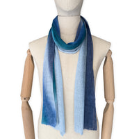 Mannequin wearing a colorful and lightweight linen scarf on a white background. Linen scarf is in shades of blue, midnight blue, light blue, turquoise and indigo colors. It is hand-painted scarf in measures 32 x 200 cm by otta-italy scarves brand. Luxury Italian linen, soft and lightweight scarf for women and men.