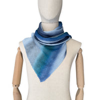 Mannequin wearing a colorful and lightweight linen scarf on a white background. Linen scarf is in shades of blue, midnight blue, light blue, turquoise and indigo colors. It is hand-painted scarf in measures 32 x 200 cm by otta-italy scarves brand. Luxury Italian linen, soft and lightweight scarf for women and men.