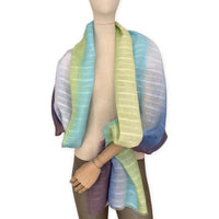 Mannequin wearing a hand-painted Otta pure linen scarf on a white background in 
blue, turquoise, green and purple tones. soft, fresh and lightweight, and elegant accessory measuring 70 x 190 cm. Unique artisan scarf with hand-sewn edges, perfect for women and men.

