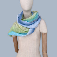
Mannequin wearing scarf on a pastel blue background. Hand-painted linen scarf by Otta-Italy, 70 x 190 cm, featuring 
blue, turquoise, green and purple. Luxury Italian pure linen accessory, soft, fresh and lightweight scarf for women and men.
