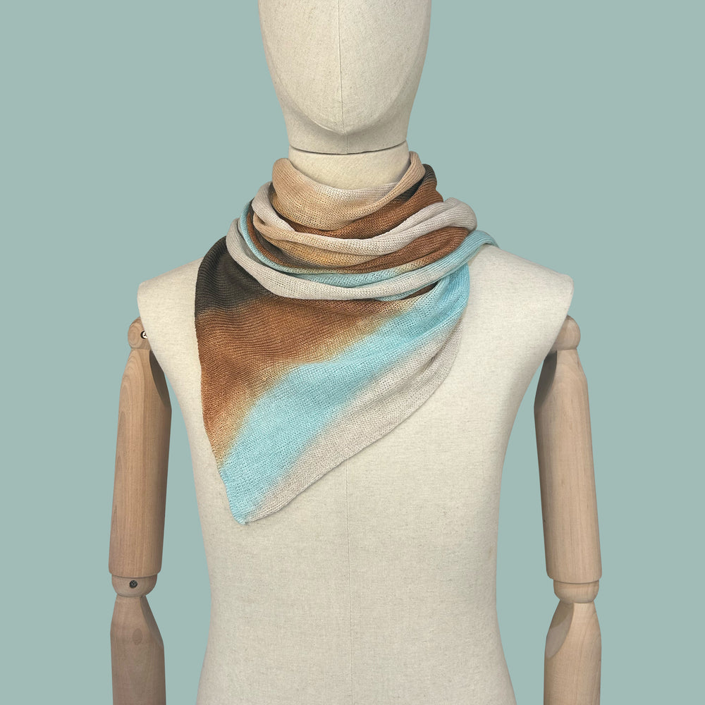 Mannequin wearing a hand-painted pure linen scarf by Otta-Italy, blue background. Brown, gray and light blue. 38x196 cm.

