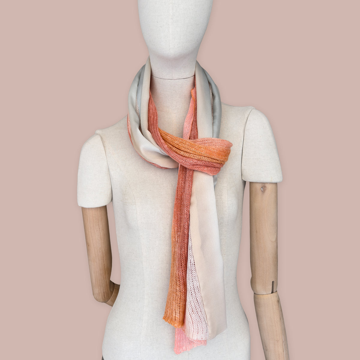 Mannequin wearing scarf on a pastel pink background. Hand-painted linen scarf by Otta-Italy, 37 x 196 cm, featuring 
coral, orange, gray, and champagne. Luxury Italian pure linen accessory, soft, fresh and lightweight scarf for women and men.
