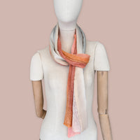 Mannequin wearing scarf on a pastel pink background. Hand-painted linen scarf by Otta-Italy, 37 x 196 cm, featuring 
coral, orange, gray, and champagne. Luxury Italian pure linen accessory, soft, fresh and lightweight scarf for women and men.
