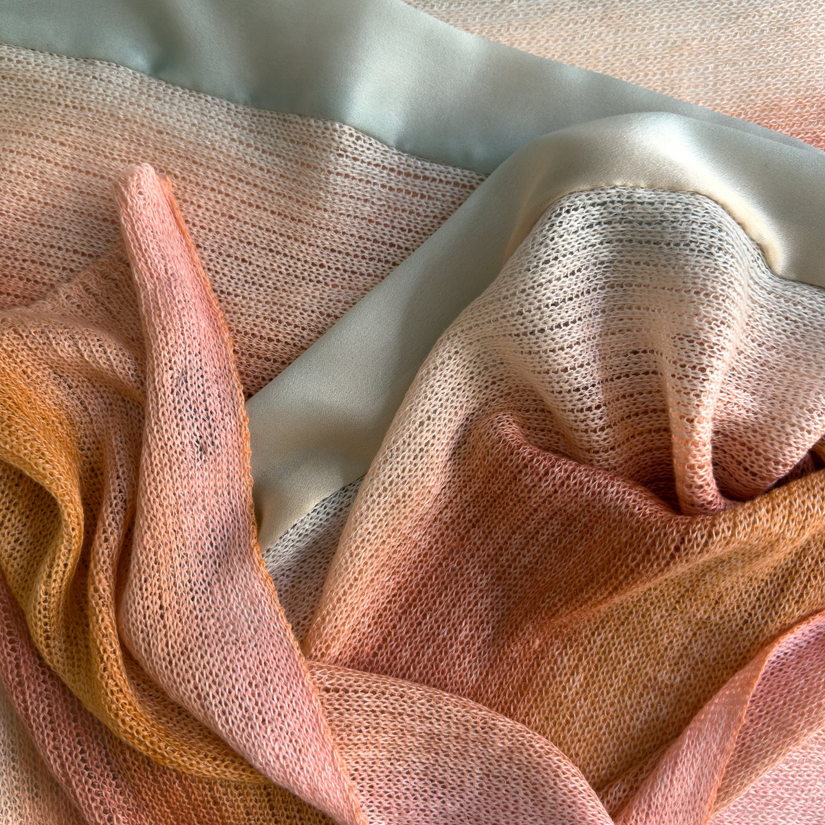 Mannequin wearing scarf on a pastel pink background. Hand-painted linen scarf by Otta-Italy, 37 x 196 cm, featuring 
coral, orange, gray, and champagne. Luxury Italian pure linen accessory, soft, fresh and lightweight scarf for women and men.
