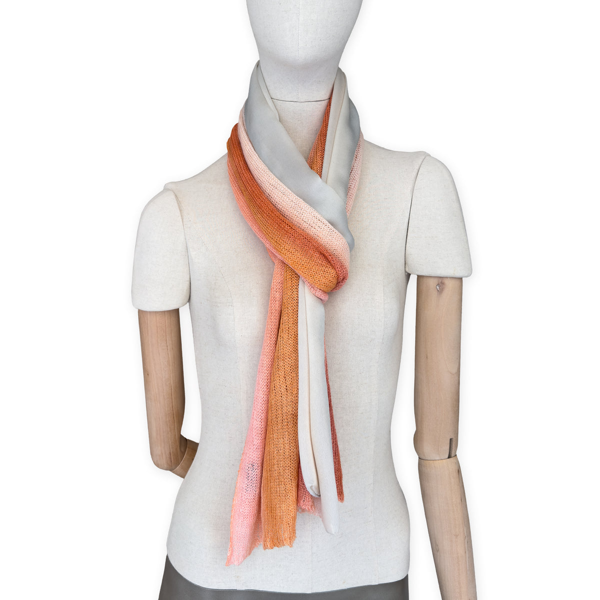 Mannequin wearing a hand-painted Otta pure linen scarf on a white background in 
coral, orange, gray, and champagne tones. soft, fresh and lightweight, and elegant accessory measuring 37 x 196 cm. Unique artisan scarf with hand-sewn edges, perfect for women and men.
