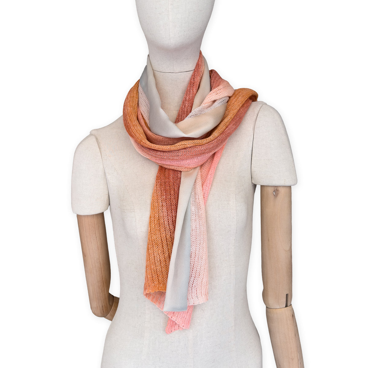 Mannequin wearing a hand-painted Otta pure linen scarf on a white background in 
coral, orange, gray, and champagne tones. soft, fresh and lightweight, and elegant accessory measuring 37 x 196 cm. Unique artisan scarf with hand-sewn edges, perfect for women and men.
