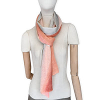 Mannequin wearing a hand-painted Otta pure linen scarf on a white background in 
coral, orange, gray, and champagne tones. soft, fresh and lightweight, and elegant accessory measuring 37 x 196 cm. Unique artisan scarf with hand-sewn edges, perfect for women and men.

