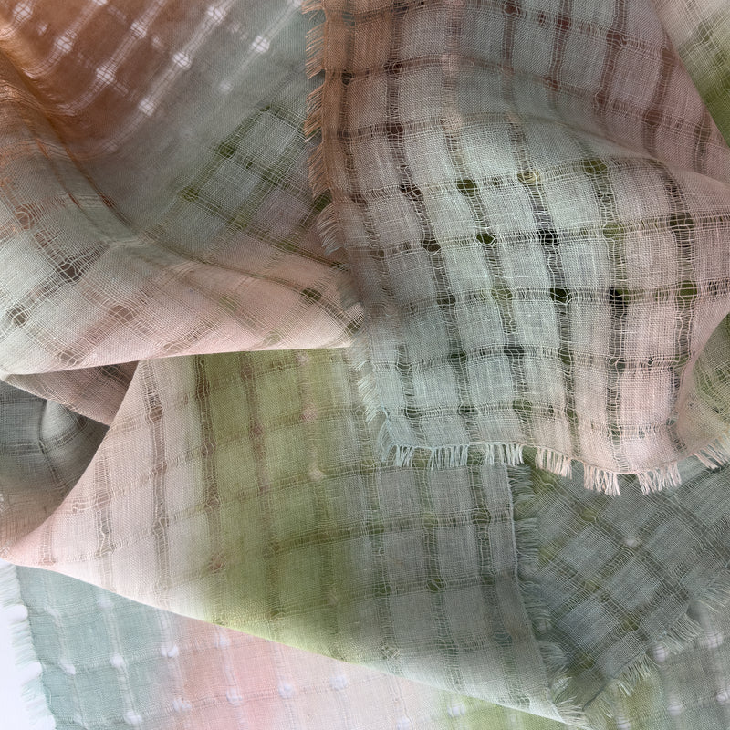 Close-up of soft fabric, a hand-painted Otta pure linen scarf draped softly, showcasing gentle shades of 
green and beigen. Lightweight artisan accessory with delicate hand-sewn edges, measuring 48 x 190 cm.
