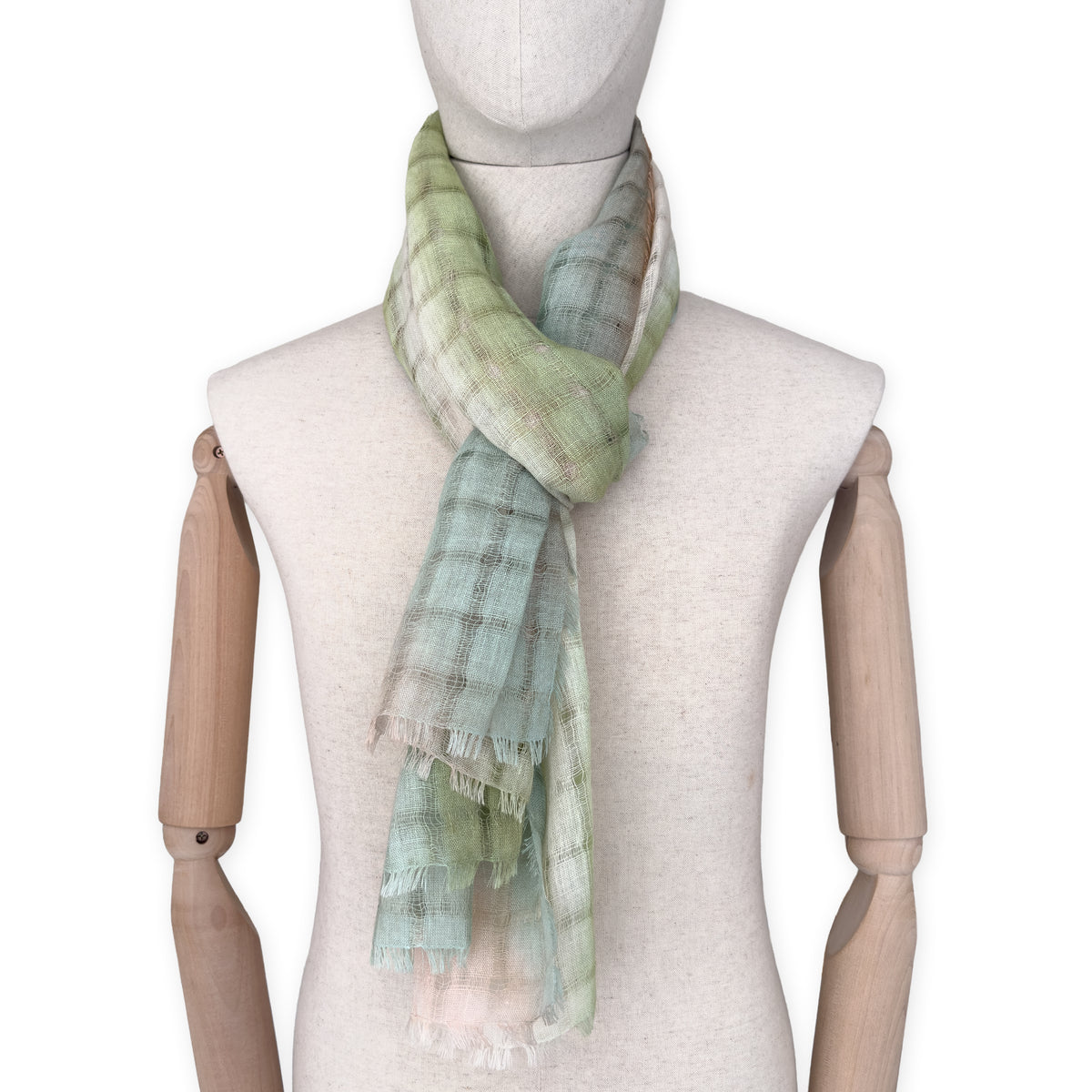 Mannequin wearing a hand-painted Otta pure linen scarf on a white background in 
green and beige tones. soft, fresh and lightweight, and elegant accessory measuring 48 x 190 cm. Unique artisan scarf with hand-sewn edges, perfect for women and men.