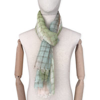 Mannequin wearing a hand-painted Otta pure linen scarf on a white background in 
green and beige tones. soft, fresh and lightweight, and elegant accessory measuring 48 x 190 cm. Unique artisan scarf with hand-sewn edges, perfect for women and men.