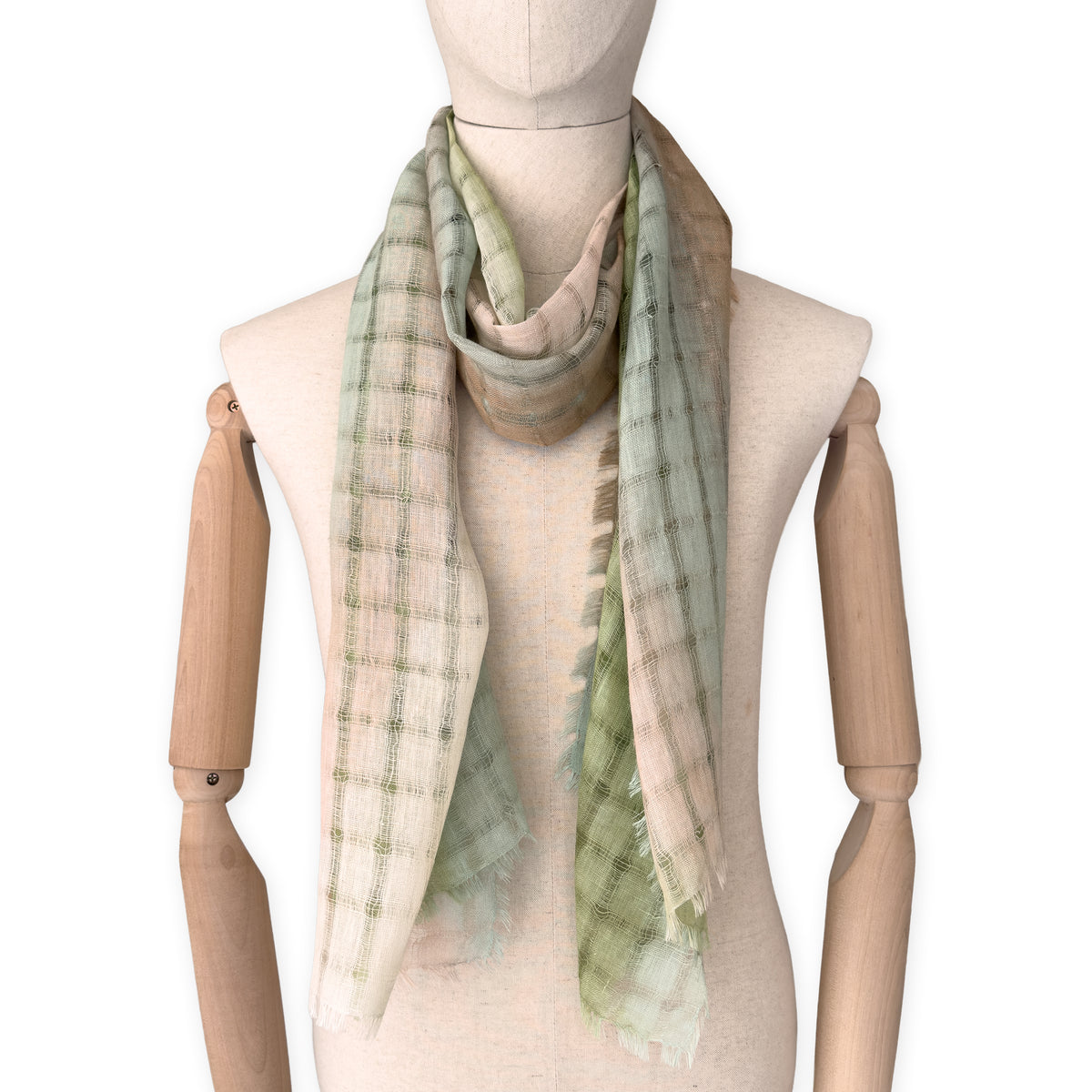 Mannequin wearing a hand-painted Otta pure linen scarf on a white background in 
green and beige tones. soft, fresh and lightweight, and elegant accessory measuring 48 x 190 cm. Unique artisan scarf with hand-sewn edges, perfect for women and men.