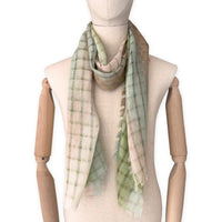 Mannequin wearing a hand-painted Otta pure linen scarf on a white background in 
green and beige tones. soft, fresh and lightweight, and elegant accessory measuring 48 x 190 cm. Unique artisan scarf with hand-sewn edges, perfect for women and men.
