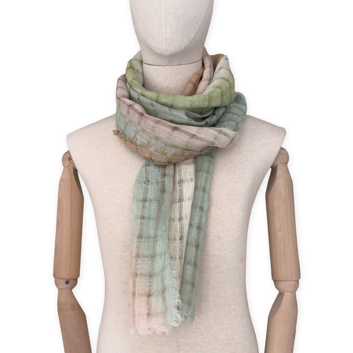 Mannequin wearing a hand-painted Otta pure linen scarf on a white background in 
green and beige tones. soft, fresh and lightweight, and elegant accessory measuring 48 x 190 cm. Unique artisan scarf with hand-sewn edges, perfect for women and men.