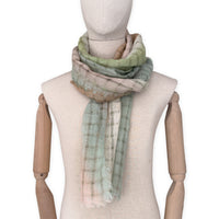 Mannequin wearing a hand-painted Otta pure linen scarf on a white background in 
green and beige tones. soft, fresh and lightweight, and elegant accessory measuring 48 x 190 cm. Unique artisan scarf with hand-sewn edges, perfect for women and men.