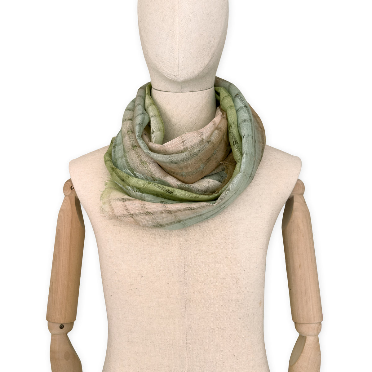 Mannequin wearing a hand-painted Otta pure linen scarf on a white background in 
green and beige tones. soft, fresh and lightweight, and elegant accessory measuring 48 x 190 cm. Unique artisan scarf with hand-sewn edges, perfect for women and men.