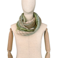 Mannequin wearing a hand-painted Otta pure linen scarf on a white background in 
green and beige tones. soft, fresh and lightweight, and elegant accessory measuring 48 x 190 cm. Unique artisan scarf with hand-sewn edges, perfect for women and men.
