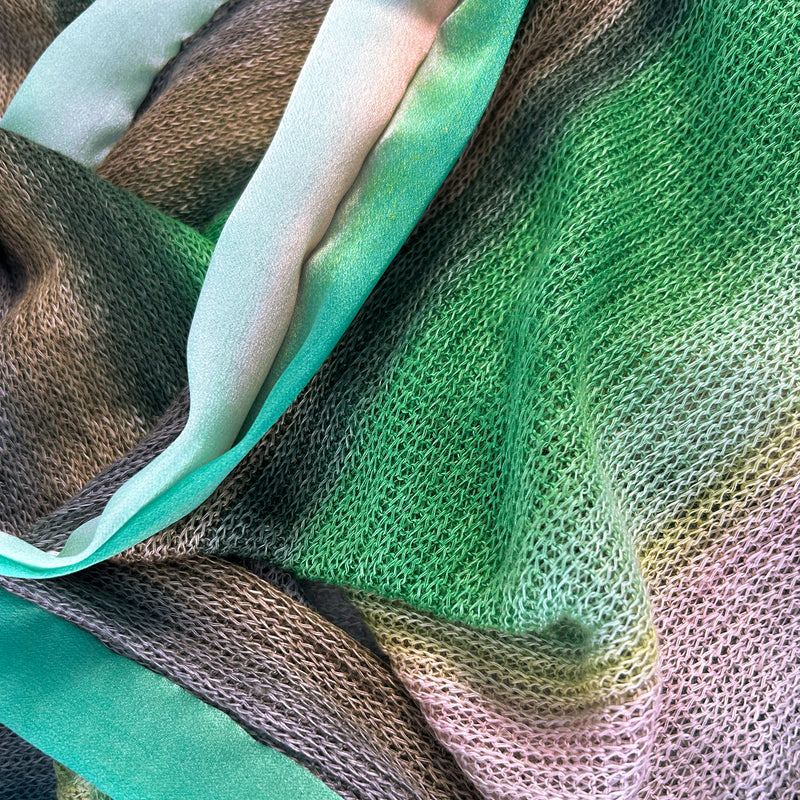 Close-up of a hand-painted Otta-Italy Florentine knit linen scarf showcasing the fine contrast between the textured emerald green knit body and the smooth, hand-finished pure silk border.