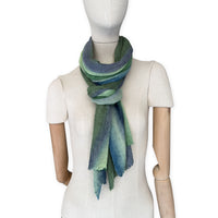 Mannequin wearing a colorful and lightweight linen scarf on a white background. Linen scarf is in shades of green and blue colors. It is hand-painted scarf in measures 35 x 202 cm by otta-italy scarves brand. Luxury Italian linen, soft and lightweight scarf for women and men.