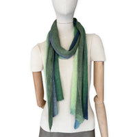 Mannequin wearing a colorful and lightweight linen scarf on a white background. Linen scarf is in shades of green and blue colors. It is hand-painted scarf in measures 35 x 202 cm by otta-italy scarves brand. Luxury Italian linen, soft and lightweight scarf for women and men.