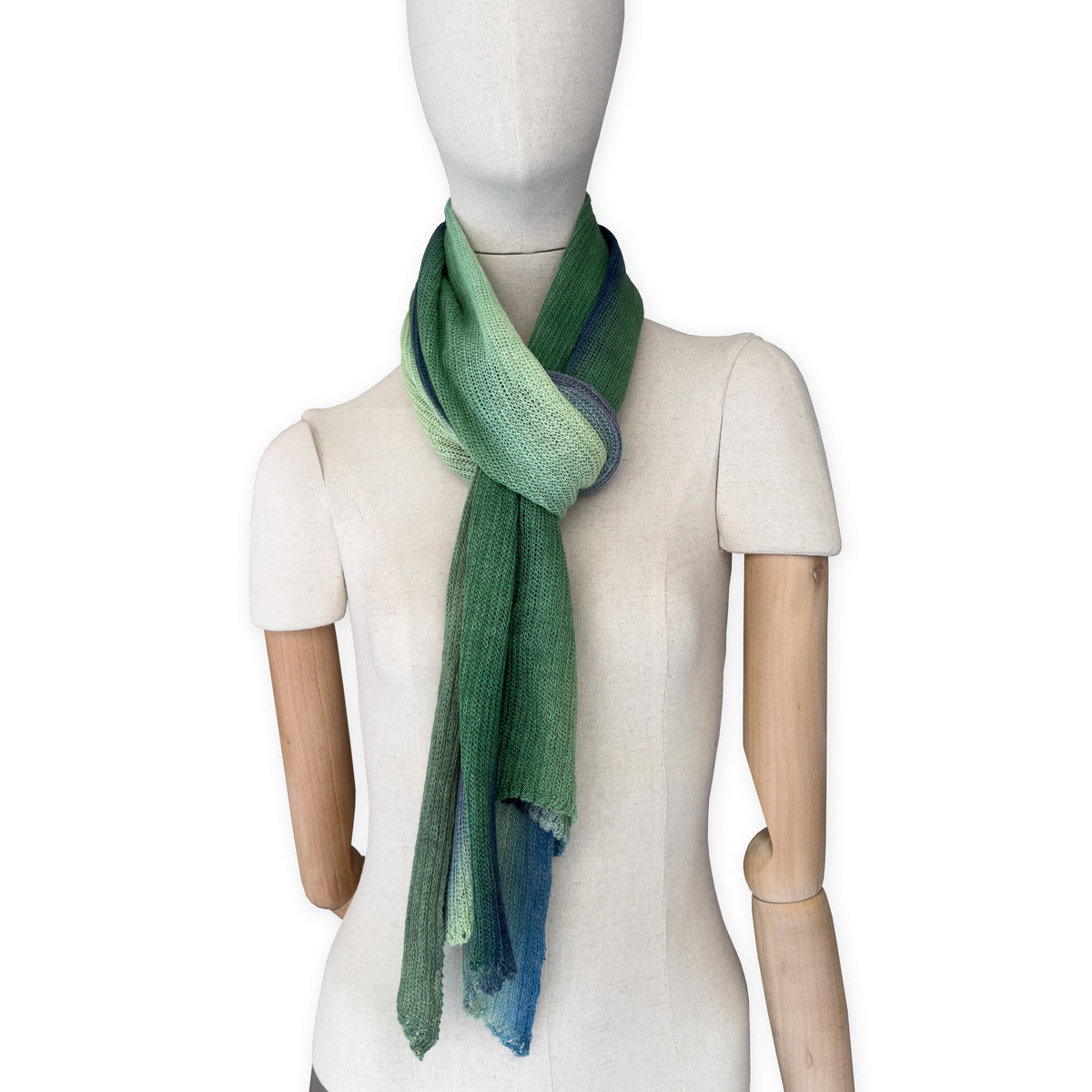 Mannequin wearing a colorful and lightweight linen scarf on a white background. Linen scarf is in shades of green and blue colors. It is hand-painted scarf in measures 35 x 202 cm by otta-italy scarves brand. Luxury Italian linen, soft and lightweight scarf for women and men.