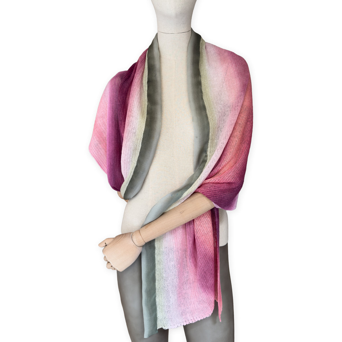 Mannequin wearing a hand-painted Otta pure linen scarf on a white background in 
pink and green tones. soft, fresh and lightweight, and elegant accessory measuring 42 x 196 cm. Unique artisan scarf with hand-sewn edges, perfect for women and men.
