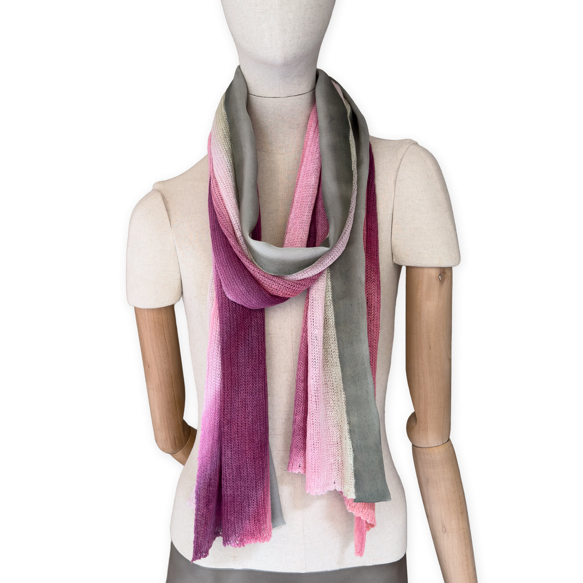 Mannequin wearing a hand-painted Otta pure linen scarf on a white background in 
pink and green tones. soft, fresh and lightweight, and elegant accessory measuring 42 x 196 cm. Unique artisan scarf with hand-sewn edges, perfect for women and men.
