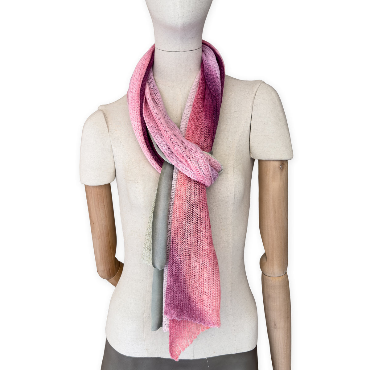 Mannequin wearing a hand-painted Otta pure linen scarf on a white background in 
pink and green tones. soft, fresh and lightweight, and elegant accessory measuring 42 x 196 cm. Unique artisan scarf with hand-sewn edges, perfect for women and men.
