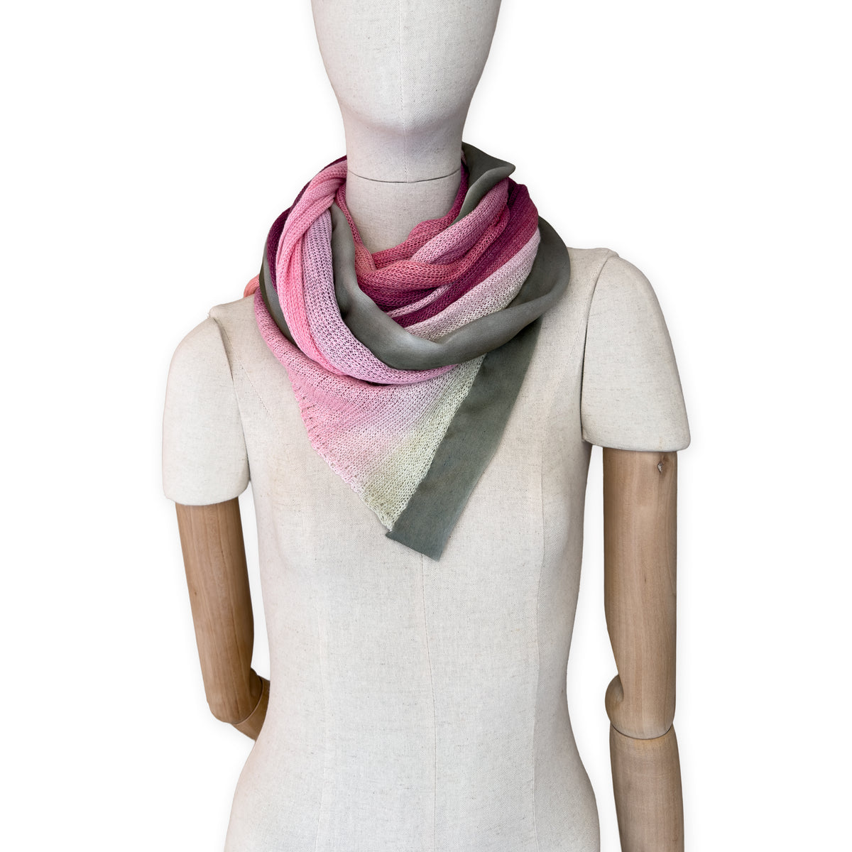 Mannequin wearing a hand-painted Otta pure linen scarf on a white background in 
pink and green tones. soft, fresh and lightweight, and elegant accessory measuring 42 x 196 cm. Unique artisan scarf with hand-sewn edges, perfect for women and men.
