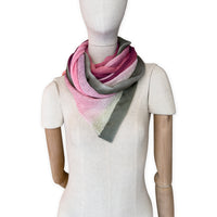 Mannequin wearing a hand-painted Otta pure linen scarf on a white background in 
pink and green tones. soft, fresh and lightweight, and elegant accessory measuring 42 x 196 cm. Unique artisan scarf with hand-sewn edges, perfect for women and men.
